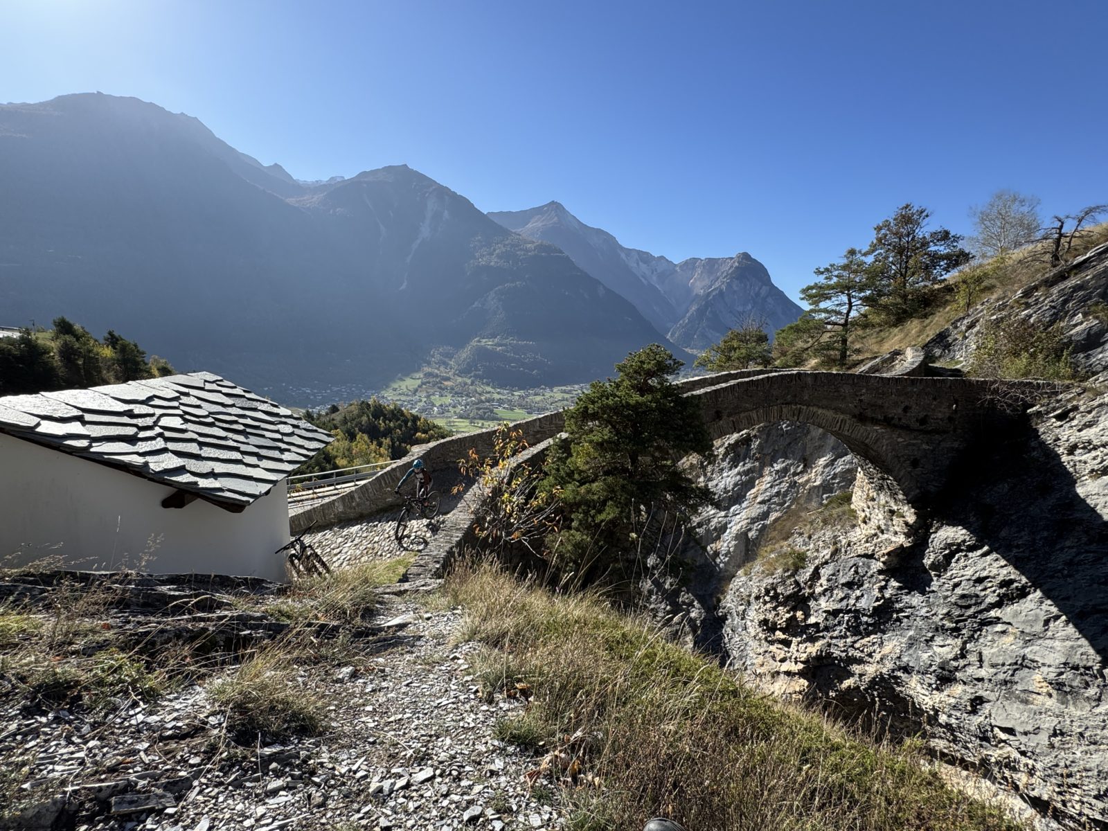 Mountainbiker fährt über eine alte Brücke aus Stein im Wallis, Schweiz. Erlebe tolle Touren an einem der Brückentage 2025
